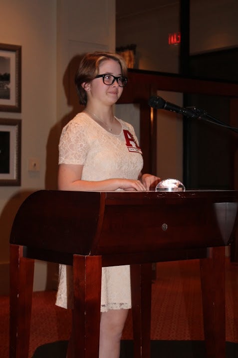 Lady in white dress standing behind podium in dim light room.