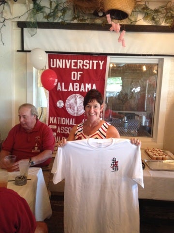 Man in red shirt and lady holding white t-shirt in room with red/white University Banner in background.