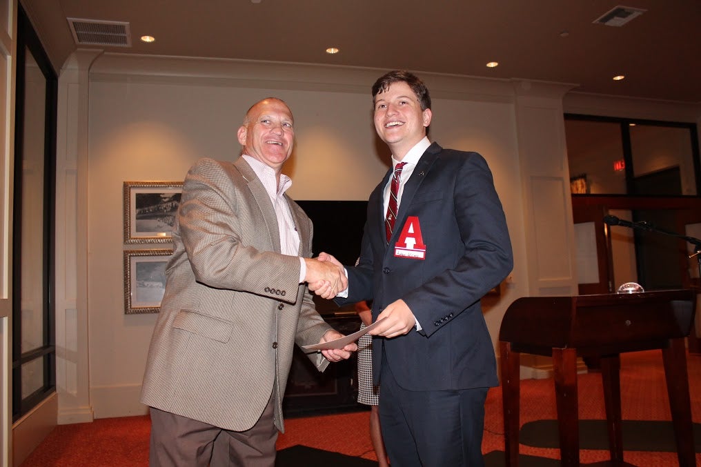 Dean Chuck Karr shaking hands with man in dark suite in front of white wall.