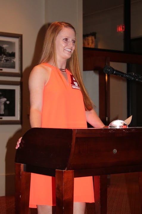Student in orange dress standing behind podium.