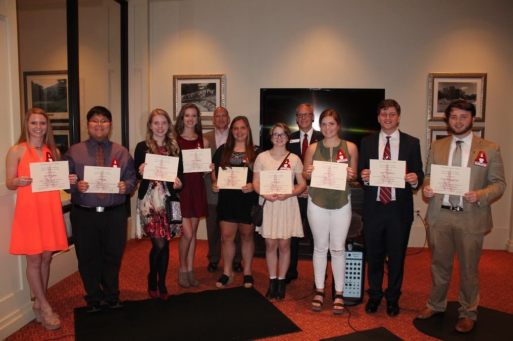 Group of students holding certificates in room with white wall.