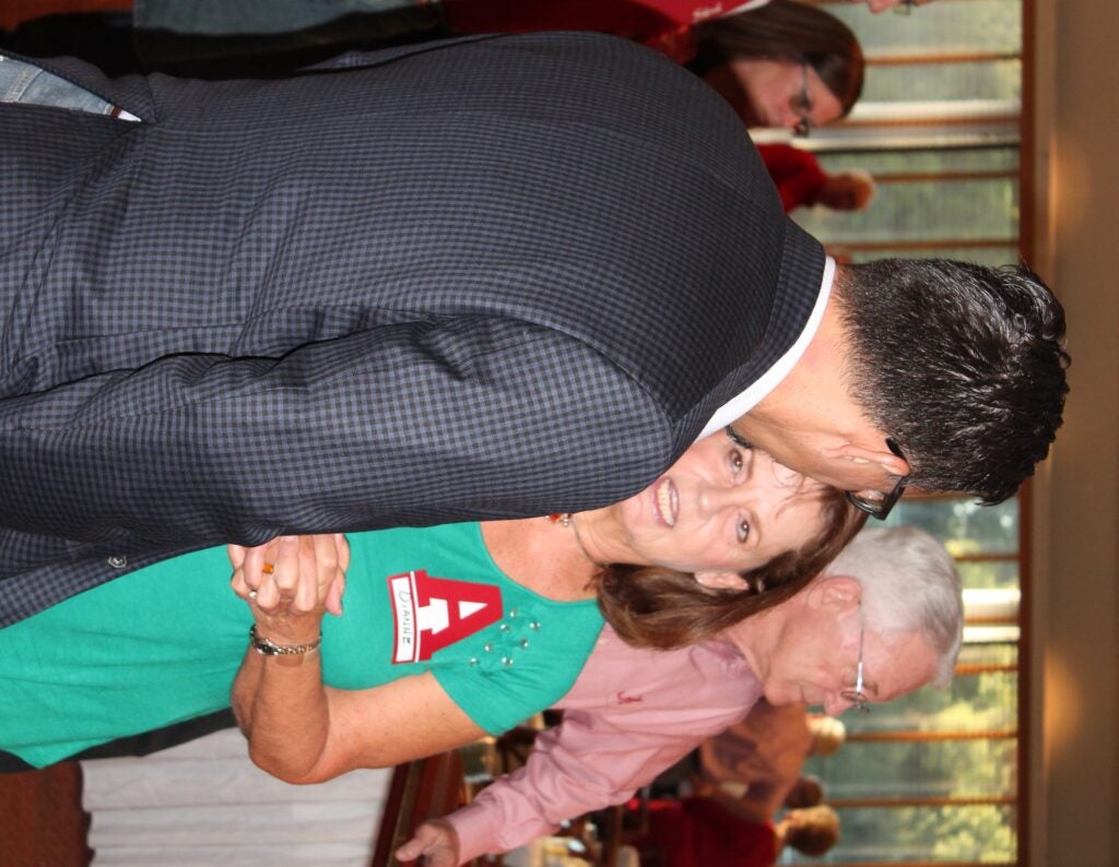 Man in dark coat talking to lady in green top with people in background.