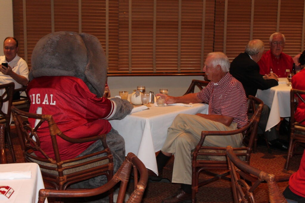 Big Al and man sitting at table in room with brown shades.