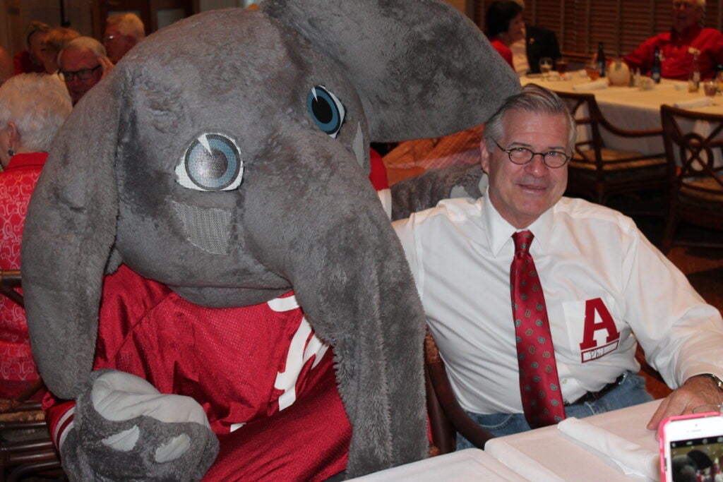 Big Al Elephant and man in white shirt and red tie siting at table.