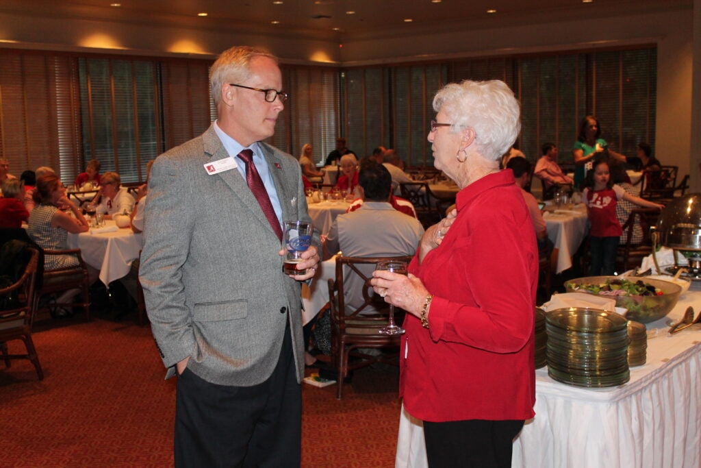 Alex Smith talking to lady in red top in dim light room.