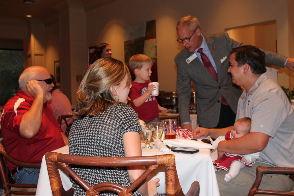 Alex Smith standing and talking to group of people at table in dim light room.
