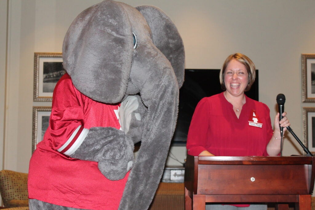 Big AL Elephant standing by lady in red shirt behind podium..
