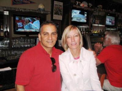 Man in red shirt and lady in white shirt sitting in front of TV Screen.