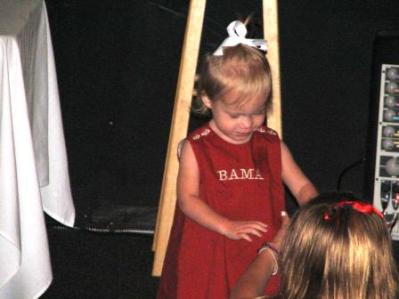 Little girl in red dress standing in dim light room.