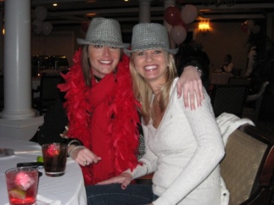 Lady in red shirt and lady in white shirt with houndstooth hats on in dim light room.