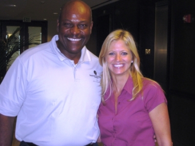 Man in white shirt and lady in purple shirt standing in dim light room.