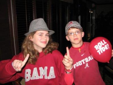 Girl in red BAMA shirt and Boy in Red Football shirt in dim light room.