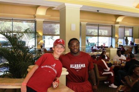 Two pepole dressed in red shirts standing in room with windows in background.