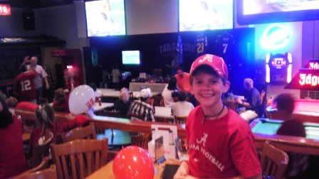 Boy in red shirt and red cap standing by a table.