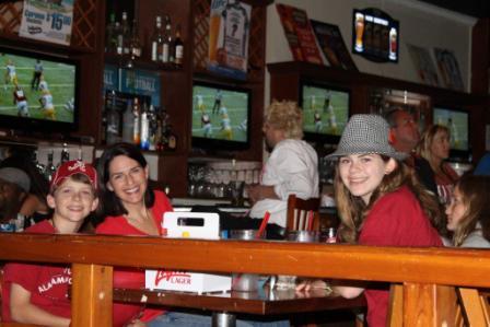 Group of people sitting in room with dim light and TV Screen in background.