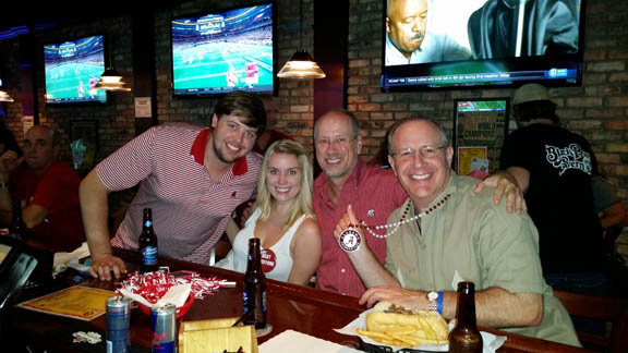 Group of people sitting at table in front of TV screen.