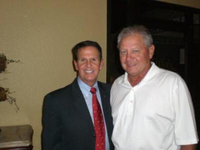 Two people standing in front of beige wall.