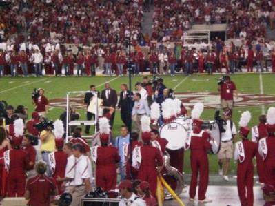 Band members on football field and fans in the background.