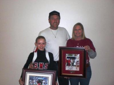 Group of people standing in room and two holding framed pictures.