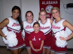 Group of Alabama Cheerleaders standing behind student in room.