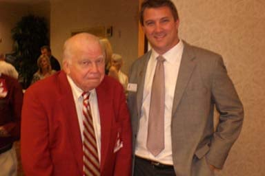 Two men standing in room with beige wall.
