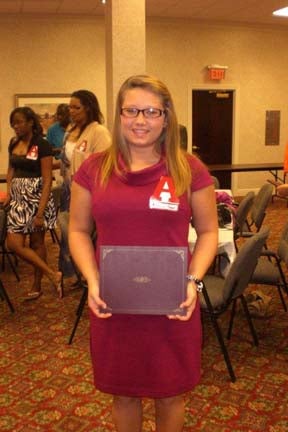 One student standing and holding a certificate and people in the background.