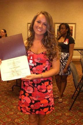 One student holding a certificate and people in the background.