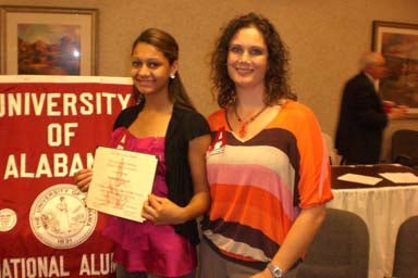 Two people standing in front of red banner and one holding a certificate.