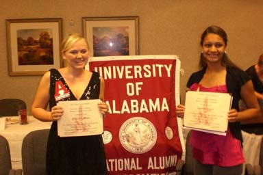 Two people standing by red banner holding certificates.