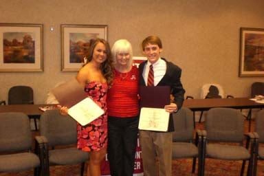 Three people standing in room with beige wall and two are holding certificates.