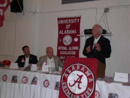One person behind podium speaking and two people sittting at table.
