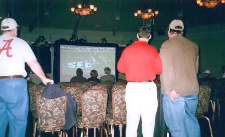 People in a dim lit room watching a football on a large tv screen