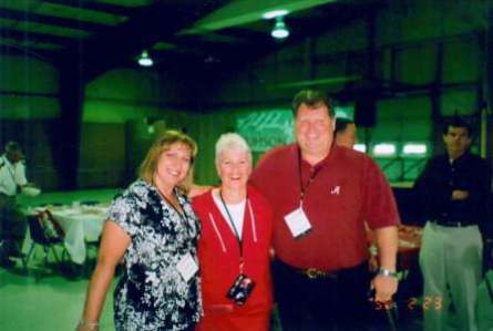 Three people standing in room with green background.
