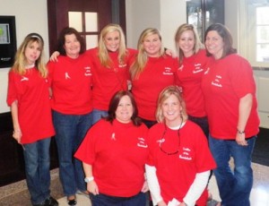 Group of people in red shirts standing in room with door in background.