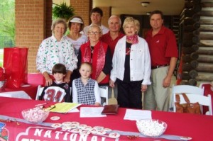 Group of people standing behind table with red cloth.