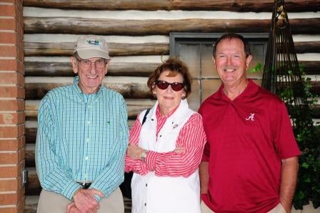 Three people standing in front of log wall.