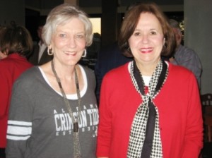 Lady in gray shirt and lady in red jacket standing in dark room.