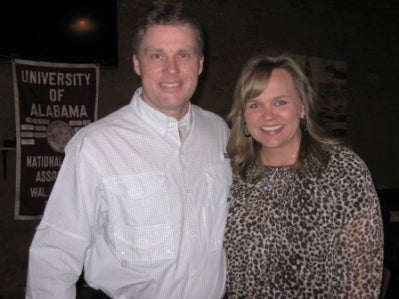 Man n white shirt and lady in black/beige dress standing in room with dark light.