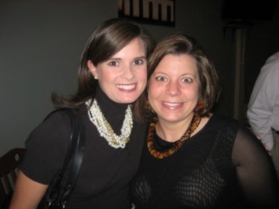 Two ladies n black dress standing in dark room.
