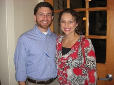 Man in blue shirt and lady in red and white top standing in front of window.