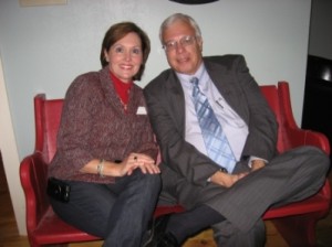 Two people sitting in red chairs with white walls in background.