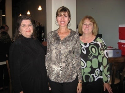 Three ladies standing in room with white and gray wall.