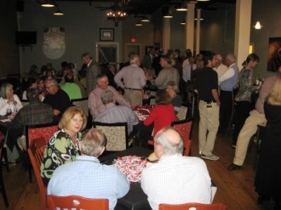 Group of people sitting at table and people standing in room with dim light.