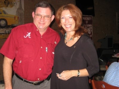 Man in red shirt and lady in black top standing in room with dim light.