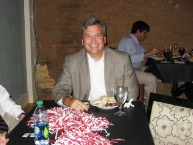 Man sitting at table with red and white shaker on table in dim light room.