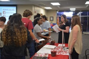 Group of people standing in front of table with red cloth.