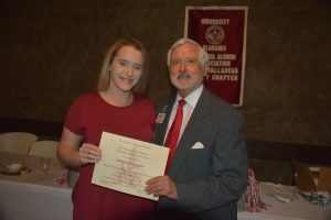 girl in red dress and man in gray suit holding certificate