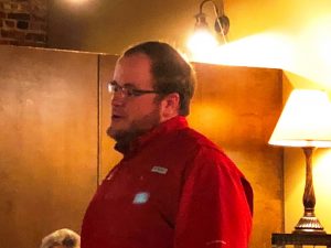 Man in red shirt standing in front of brown wall.