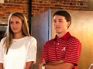 Lady in white shirt and man in red shirt standing in front of brick wall.