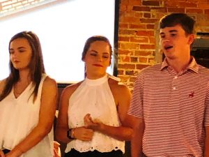 Group of people standing in front of white screen and brick wall.